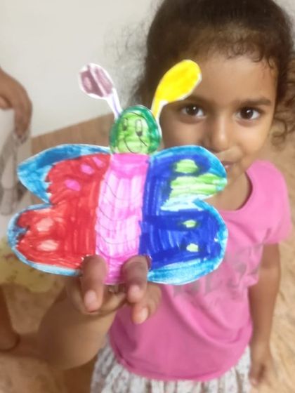 A young girl proudly shows the colorful butterfly craft she made and colored.