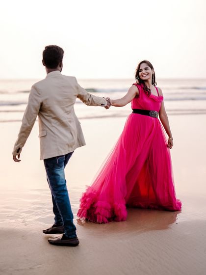 A "follow me to the sea" style shot. The pink ruffled gown looks beautiful in motion, creating a playful and romantic pre-wedding photo.