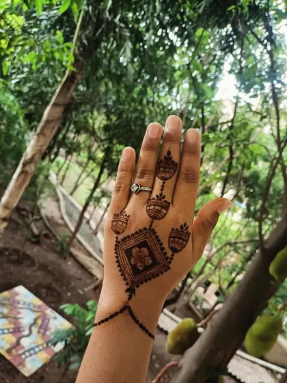 The finished jewellery-style mehendi, looking like a beautiful piece of hand adornment against a natural, green background.