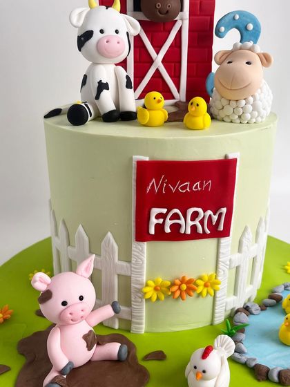 A view of the side of the farm cake, featuring the "Nivaan Farm" sign, a white picket fence, and a playful pig in the mud.