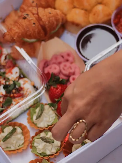 A hand reaching into our Valentine's grazing box, filled with an assortment of sweet and savory bites like asparagus tarts and caprese salad.