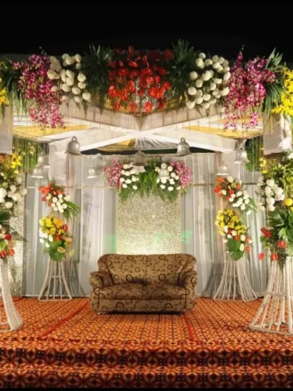 A traditional stage setup for a wedding reception, featuring a colorful explosion of flowers on a raised platform with a classic sofa for seating.