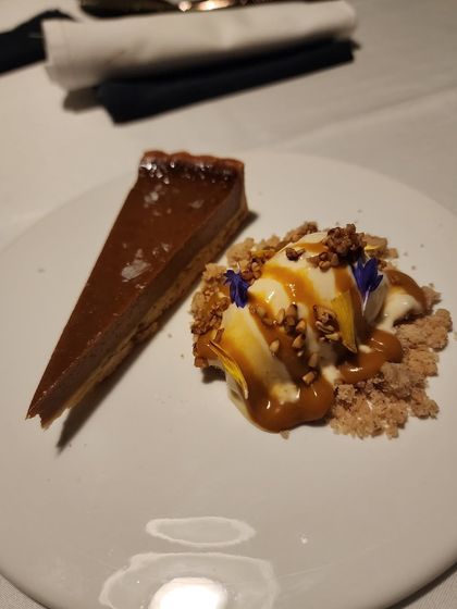 A slice of rich chocolate tart served with a scoop of vanilla ice cream, caramel sauce, and a crunchy crumble. A decadent and satisfying dessert.