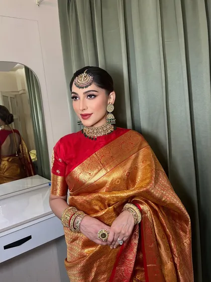 I believe in timeless elegance. This look, created for a festive occasion, features a classic red lip, sharp winged eyeliner, and a traditional pulled-back bun, perfectly complementing her beautiful golden saree.