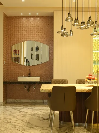 A close-up of a dining area where a rose-gold mosaic wall adds warmth and texture. The design integrates a wash basin seamlessly into the dining space, combining functionality with decorative flair under a cascade of pendant lights.
