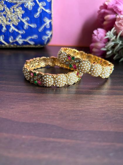 Our delicate pearl bangle collection. This pair features clusters of pearls alternating with small floral motifs made of red and green stones.