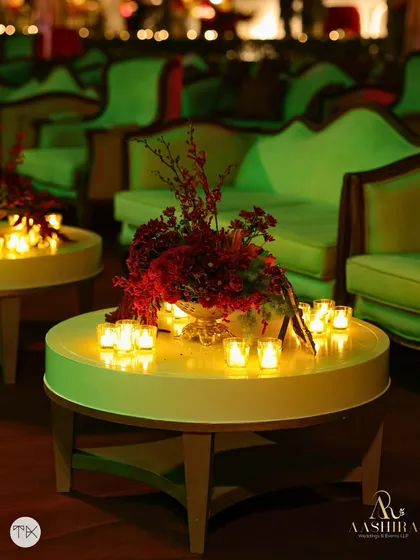 A close-up of a table centerpiece, where red florals are surrounded by a ring of glowing candles, creating an intimate and romantic atmosphere.
