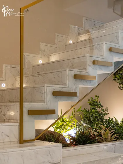 A close-up view of an under-staircase installation where light green foliage contrasts with the clean white marble. Spotlights are strategically placed to mimic sunlight and bring the artificial plants to life.