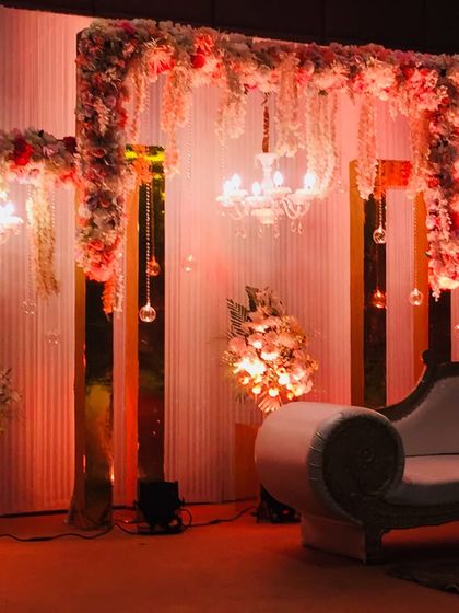 An elegant reception stage featuring golden pillars, hanging crystal tassels, and small chandeliers. The warm lighting and floral arrangements create a sophisticated and glamorous atmosphere.