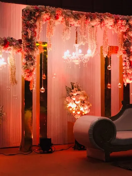 An elegant reception stage featuring golden pillars, hanging crystal tassels, and small chandeliers. The warm lighting and floral arrangements create a sophisticated and glamorous atmosphere.