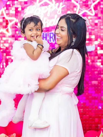 A precious moment between mother and daughter, sharing a smile against a shimmering pink backdrop at a first birthday party.