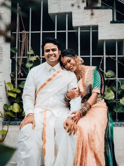 A happy portrait of a newly married couple in traditional South Indian wedding attire. The bride rests her head on her husband's shoulder, a simple gesture full of love.