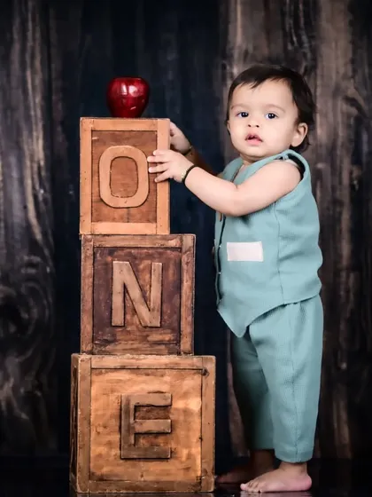 A baby boy standing next to rustic wooden "ONE" blocks, marking his first birthday.