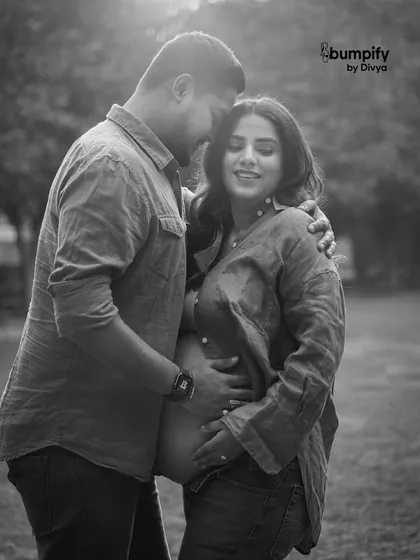 A timeless black and white portrait of a couple sharing a quiet, intimate moment outdoors. The focus is purely on their connection and the beautiful baby bump.