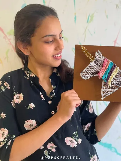 A participant proudly holds her finished unicorn string art, a whimsical and colorful creation from our workshop.