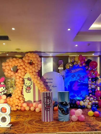 I can handle complex requests, like this joint birthday party with two different themes. On one side, a Hello Kitty and My Melody theme with pink balloons, and on the other, a Hot Wheels theme with a dynamic blue and red design, all on one stage.