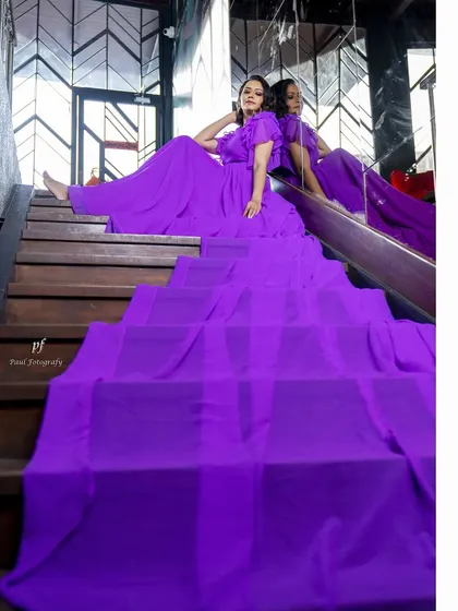 A dramatic, flowing gown in a rich purple hue, designed to create movement and elegance. The long, sweeping train and ruffled sleeves make it a perfect piece for a photoshoot or a grand entrance.