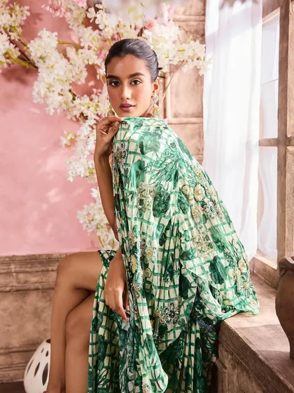 A model posing in a green printed cape and draped skirt. The makeup is kept natural and glowing to complement the fresh, botanical-inspired print.