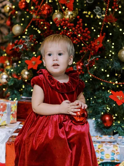 A close-up of the little girl in her red velvet dress, holding a Christmas ornament. Her expression is so sweet and thoughtful.