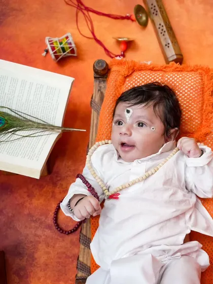 Looking up with wonder, this baby boy is styled perfectly for the Vitthal theme, with a peacock feather and holy book adding to the spiritual feel.