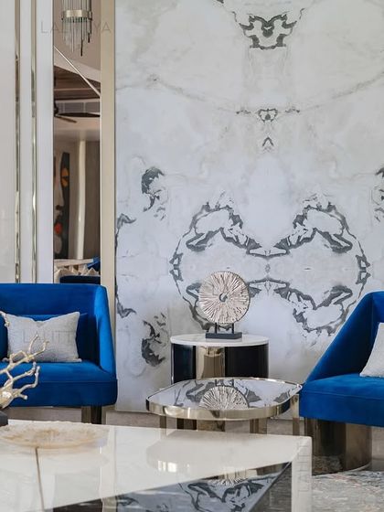 We created this conversation nook with two bold cobalt blue armchairs set against a book-matched marble feature wall. This pairing of color and pattern creates a sophisticated focal point within the larger living space.