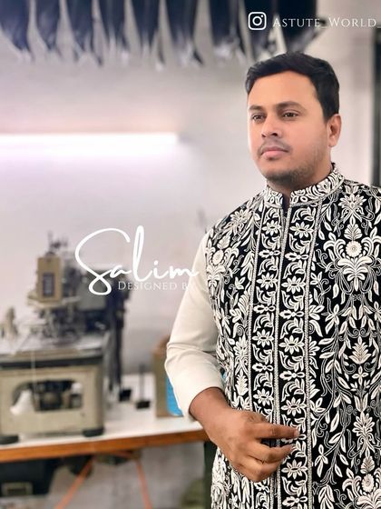 I am pictured here in my workshop, wearing a black velvet waistcoat with dense white floral embroidery over a simple white kurta, showcasing my craft.