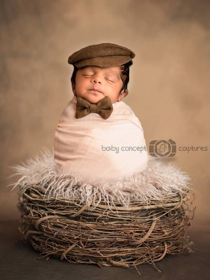 A dapper little gentleman. This newborn is dressed in a tiny bow tie and cap, posed in a soft nest for a classic and cute portrait.