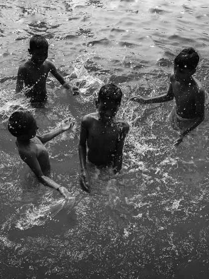 Four friends play together in the water, their joy and camaraderie captured from above in a lively black and white photograph about friendship.