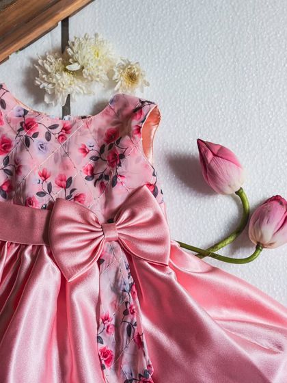 This pink satin dress features a quilted floral bodice, giving it a unique texture and depth. The large bow combines the satin and floral fabrics for a cohesive look.