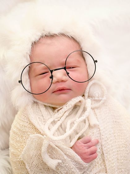 This baby looks so wise and wonderful in a fluffy white bonnet and round glasses, a simple and charming portrait.