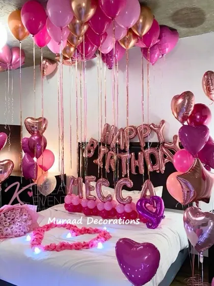 This romantic birthday setup features a canopy of pink and rose gold balloons over the bed. We also added personalized name balloons and a heart of lights for an extra special touch.