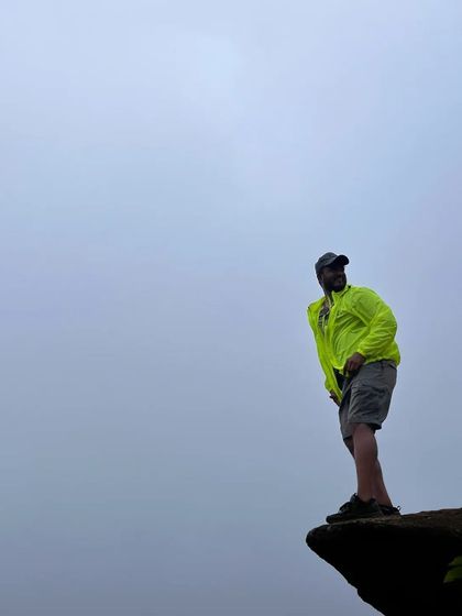 A trekker posing confidently on a cliff edge, with the foggy landscape creating a dramatic backdrop.