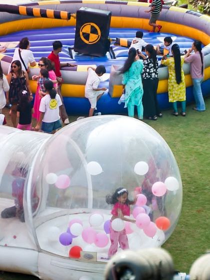 A wide view of the activity area, featuring a clear inflatable bubble house filled with balloons and a mechanical wipeout game for endless entertainment.