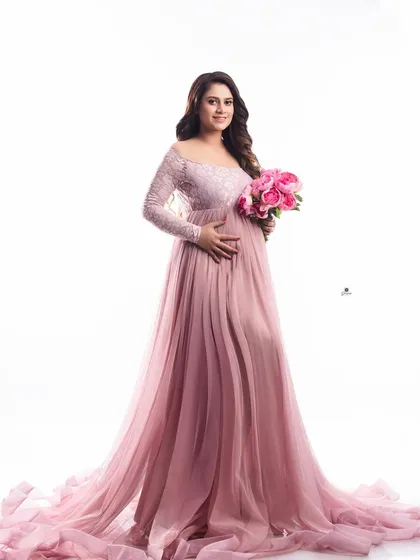 A bright and happy portrait of a mom-to-be in a beautiful pink lace gown, holding a matching bouquet. The simple white background keeps the focus on her joyful expression.