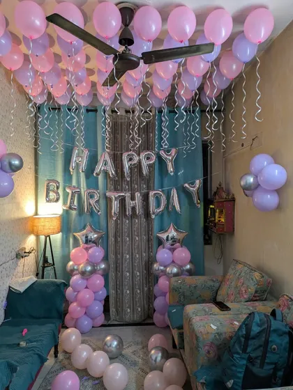 A classic birthday room setup featuring dozens of pink and purple balloons covering the ceiling, complete with silver ribbons.