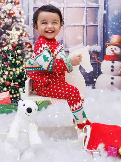 A joyful toddler in a Christmas sweater rides a rocking horse in a snowy, magical setting.