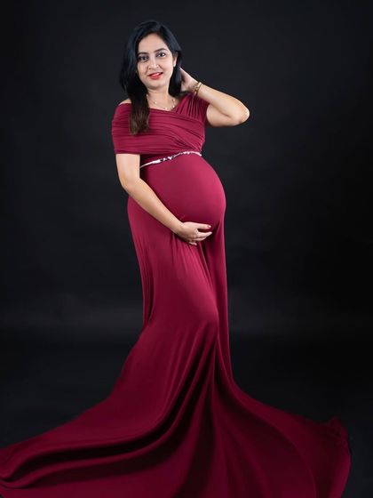 A classic portrait in a deep maroon gown with a flowing train. The simple, elegant pose against a black background puts all the focus on the expecting mother.