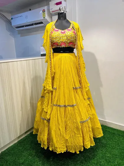 This bright yellow tiered lehenga comes with a modern twist, featuring a heavily embroidered blouse and a matching jacket with pearl detailing along the edges. It's a fun and stylish option for a Haldi function.