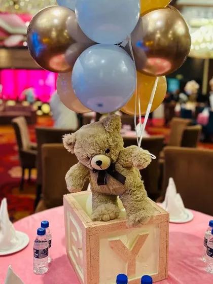 We design beautiful table centerpieces to match your theme. Here, a cute teddy bear pops out of a baby block, holding a bunch of coordinated balloons, adding a playful touch to each guest table.
