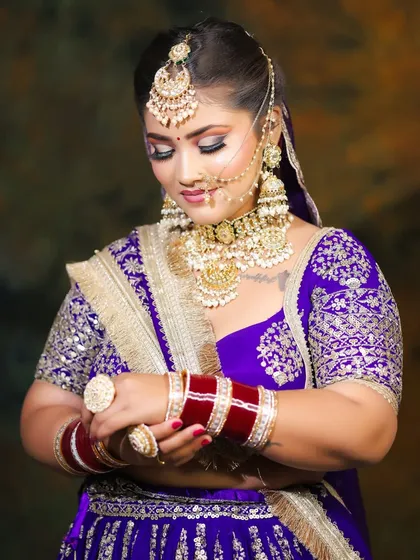 A demure bridal pose showing off the heavy embroidery and jewelry. The soft, blended makeup ensures the bride herself remains the star of the show.