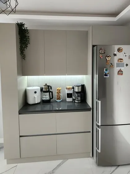 A compact and modern crockery or pantry unit in Pamposh Enclave. The design features handleless cabinets, a dark countertop for appliances, and a fluted backsplash with task lighting.