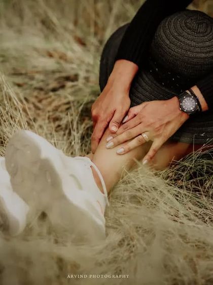 A detail shot focusing on the small things. This artistic photo captures a person's hands and sneakers nestled in tall, dry grass, creating a feeling of being grounded and connected to nature during a photoshoot.