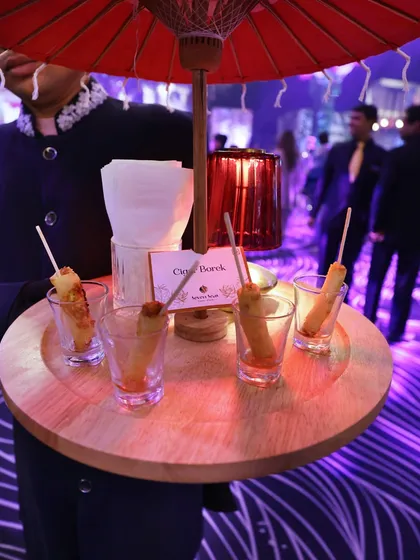 Cigar Boreks served in individual shot glasses on a wooden tray with a whimsical red umbrella. We believe in serving food with a touch of playfulness.