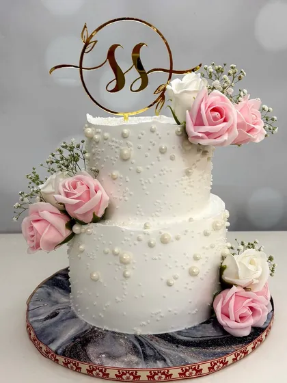 This two-tier engagement cake for 'S&S' is all about layers of magic. The design features a custom initial topper, pink and white roses, and delicate baby's breath for an unforgettable look.