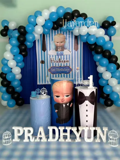 A classic Boss Baby themed party. The setup includes a blue and white striped backdrop, a balloon arch, and themed pedestals, including one designed like a tuxedo.