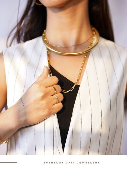 Discover the art of accessorizing with Noya. A bold gold choker is layered with a classic link chain, creating a powerful and modern statement that is effortlessly chic.