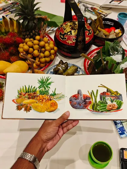 Sketching food is like tasting it twice. Here’s a spread of delicious Thai food I got to illustrate before I got to eat it. My sketchbook shows the vibrant colors of the fruits and local dishes, with the real feast right behind it, ready to be enjoyed.