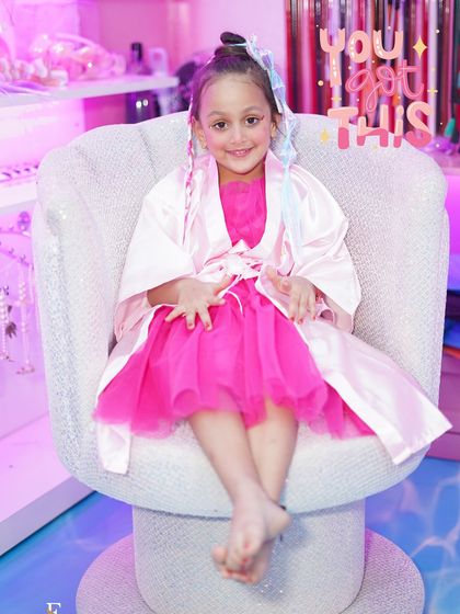 A portrait of a happy little diva. After her makeover, complete with a pink dress and colorful hair, she's all smiles in our signature sparkly armchair, ready to celebrate in style.