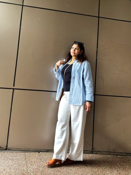 A simple and chic summer outfit. A black tank top paired with white wide-leg trousers and a light blue shirt creates a breezy and comfortable look for a sunny day.