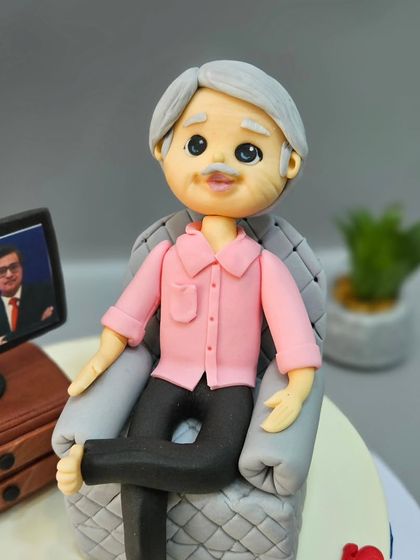 A close-up of the dad figurine for a 70th birthday cake, relaxing in his armchair and watching his favorite news channel.